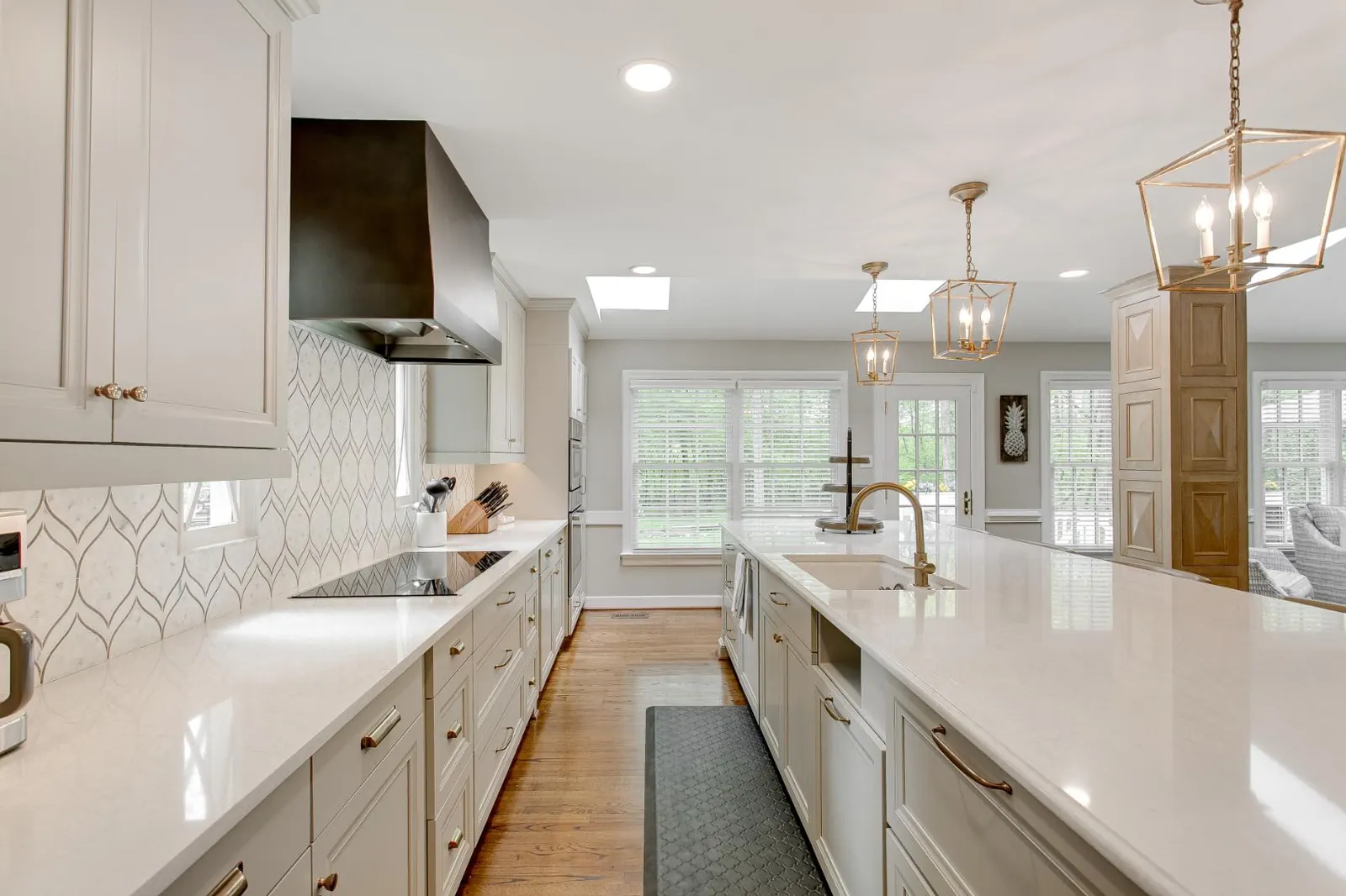 Long white kitchen with quartz countertops and brass pendant lights