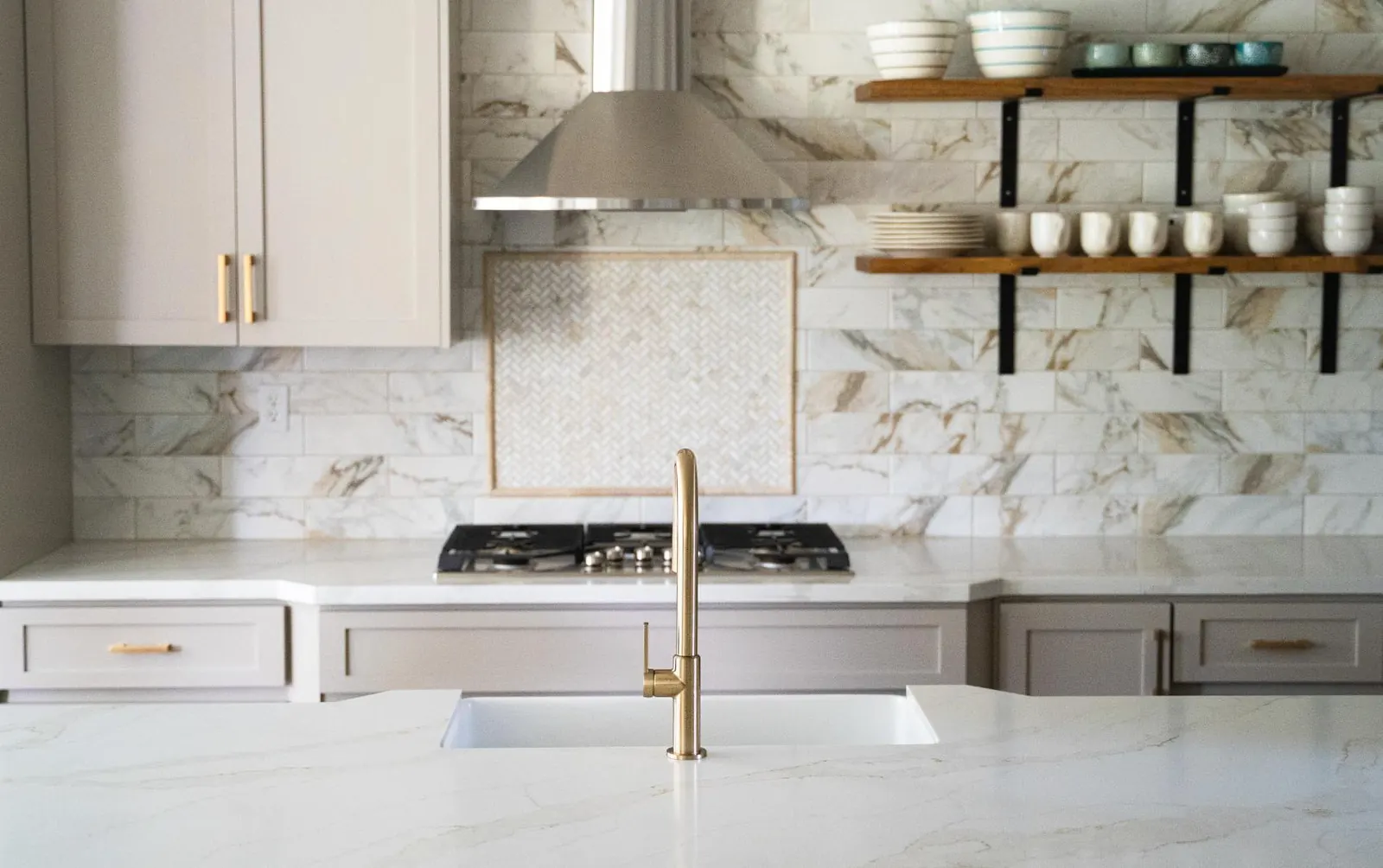 White countertop with gold-veined stone backsplash and brass faucet