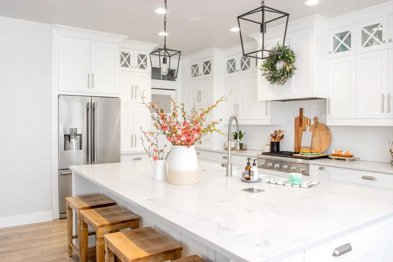 White kitchen with a large quartz island, pendant lights and wood stools